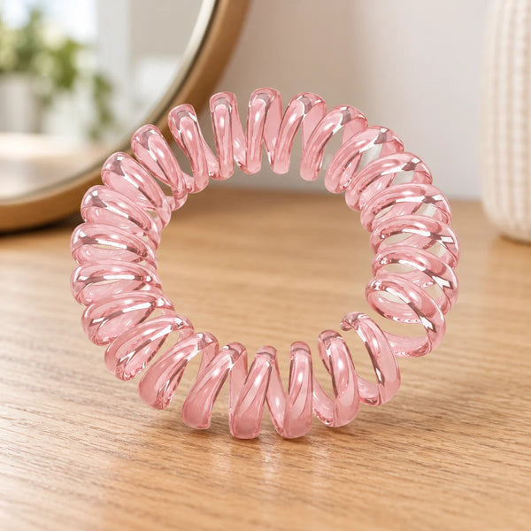 One pink coiled hair band on a wooden dressing table.
