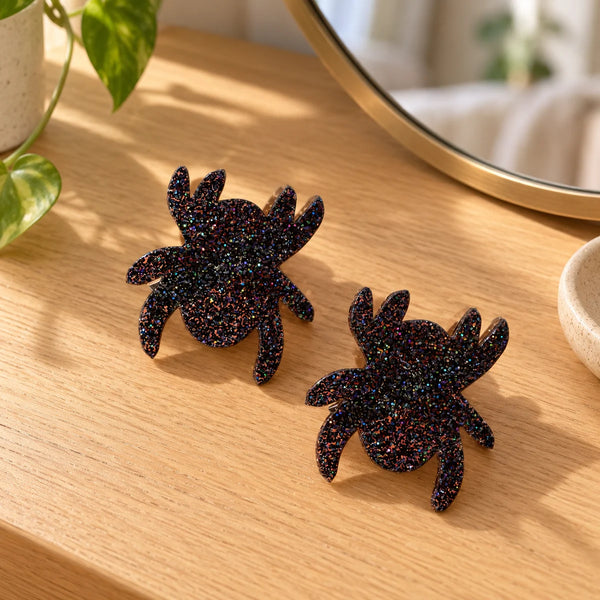 Set of two black glitter spider hair clips on a wooden dressing table.