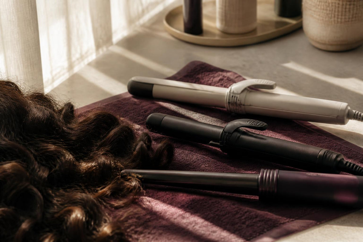 A variety of hair curling irons and wands arranged neatly on a clean white surface