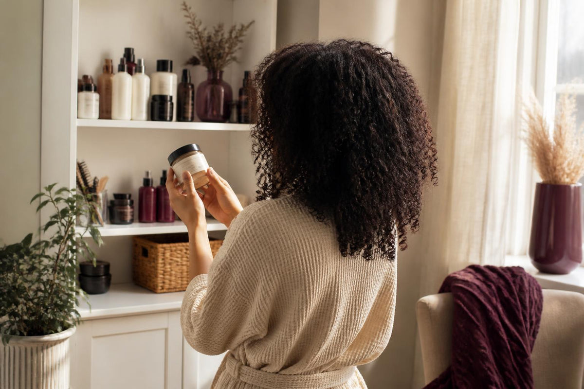 A person with textured hair smiling while holding a bottle of hair product in a bright, modern bathroom