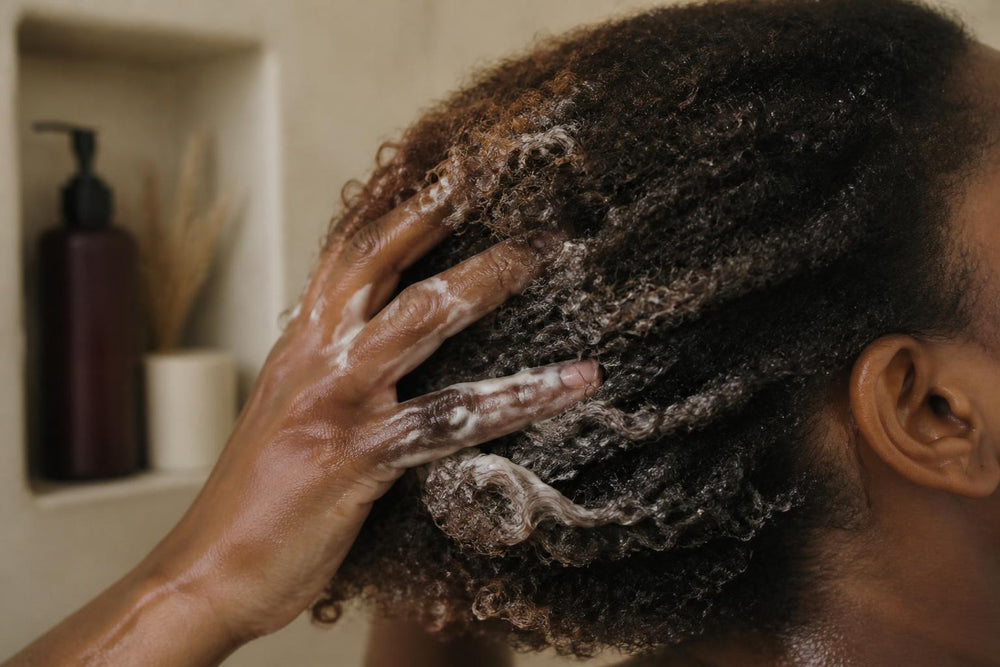 Close-up of a person with textured hair touching their curls in a bright, minimalist bathroom setting
