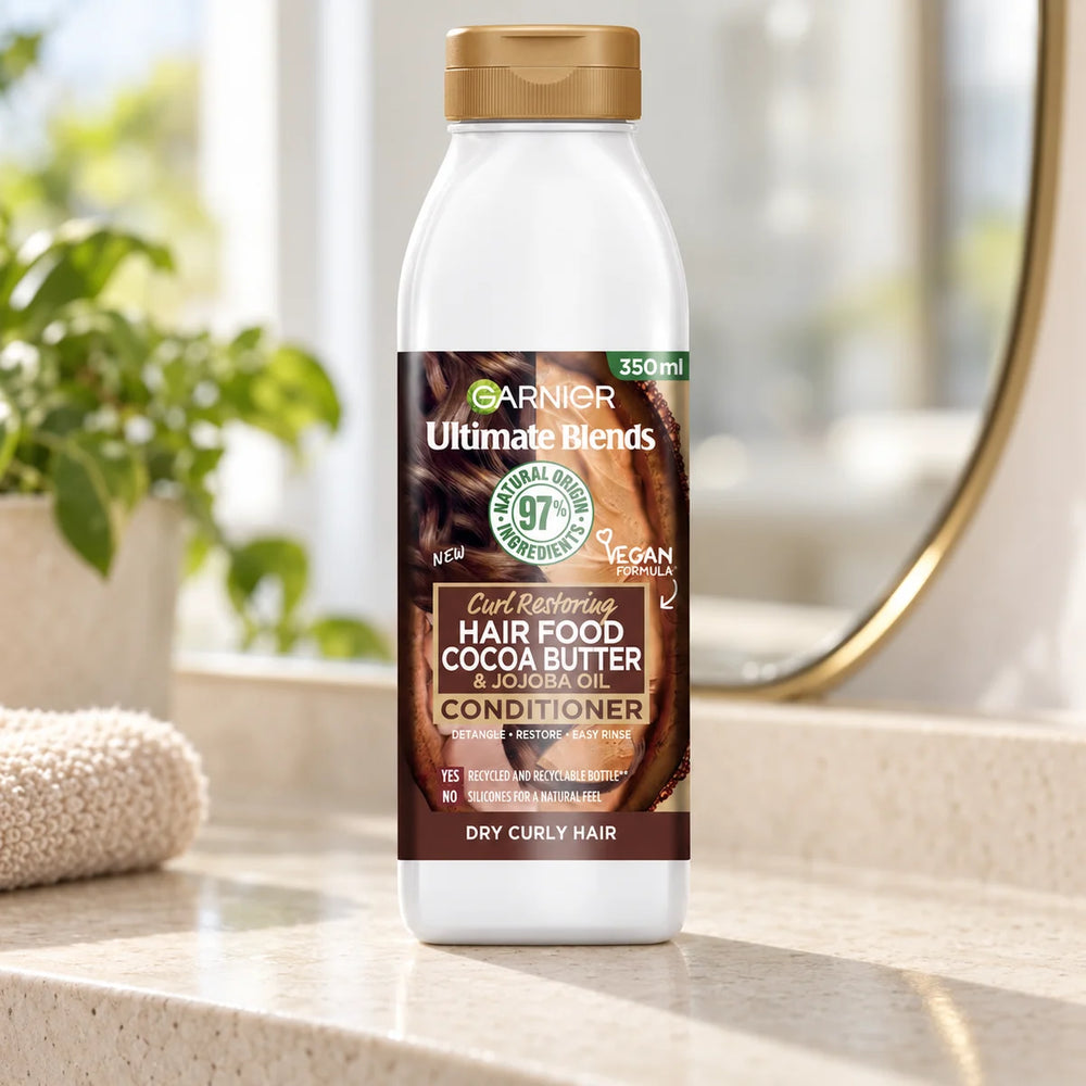 Garnier Hair Food Cocoa Butter & Jojoba Oil Conditioner Deeply Nourishing & Repairing for Dry, Frizzy & Damaged Hair — 350 ml on a bathroom vanity.