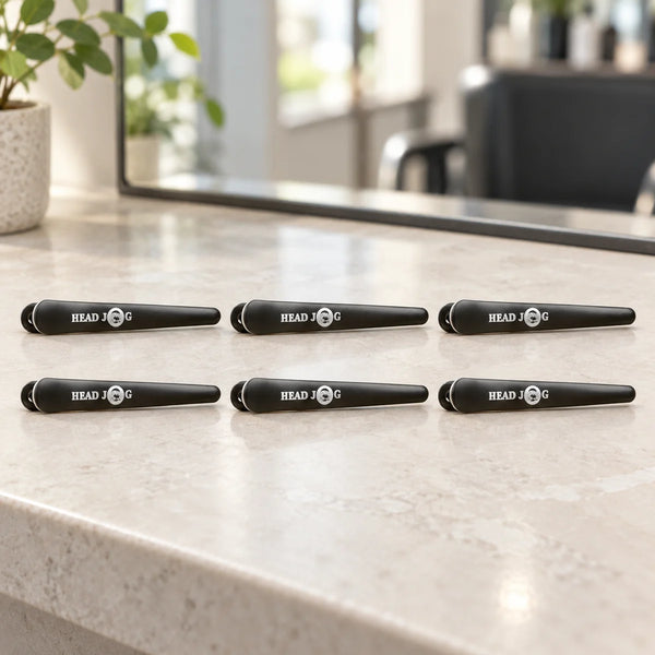 Head Jog Klip-Itz Sectioning Clips — Six black Head Jog Klip-Itz sectioning clips on a salon counter.