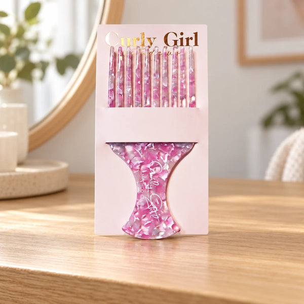Pink acetate pick comb with its source card on a wooden dressing table.