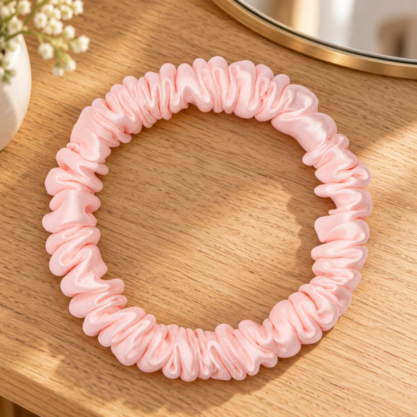 Skinny pink silk scrunchie on a wooden dressing table.